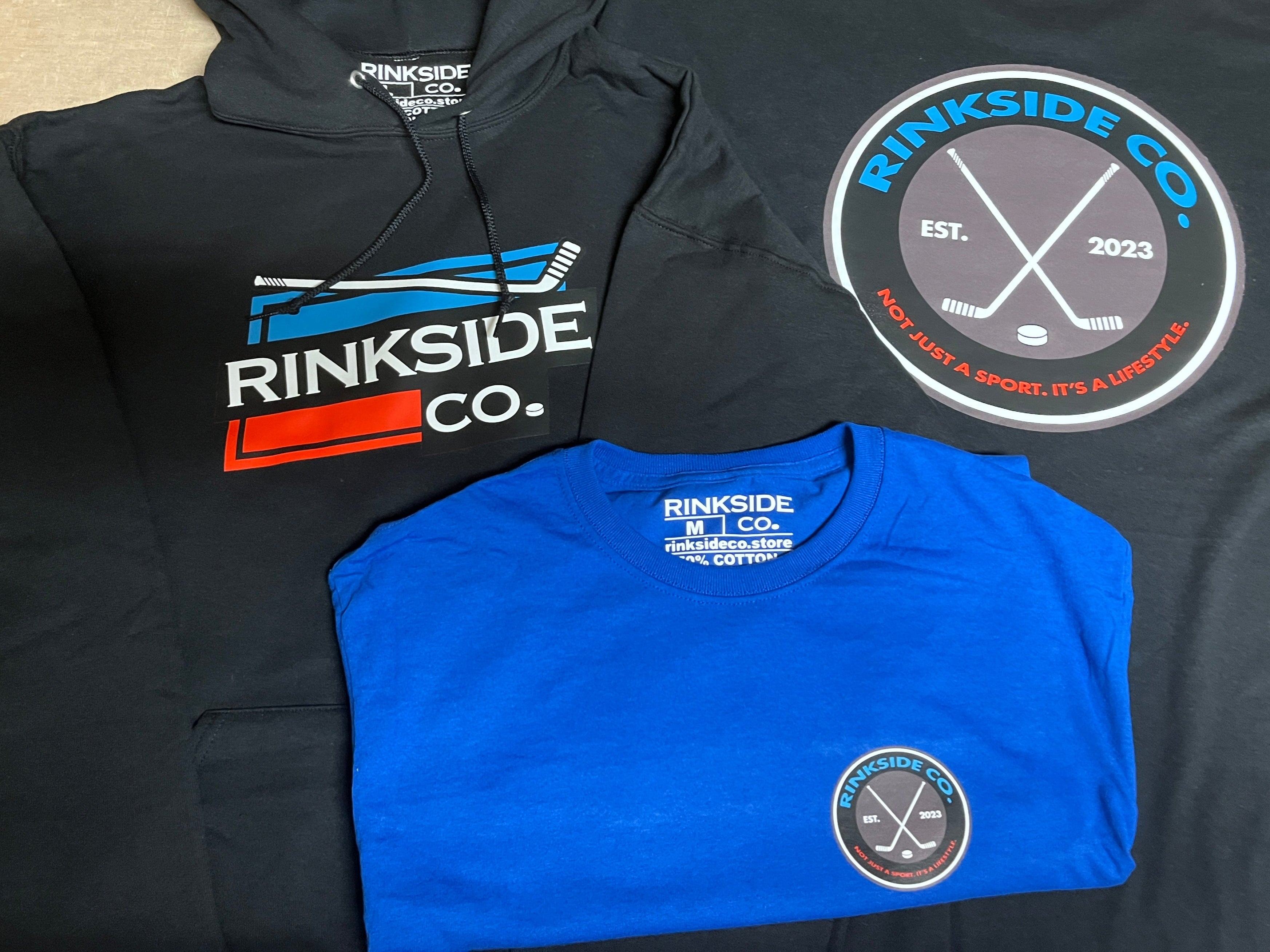 Black hoodie and blue and black t-shirts with 'Rinkside Co.' branding on a light wooden surface.